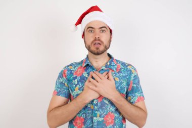 Noel Baba şapkalı genç adam korkmuş bir ifadeyle bakıyor, ellerini göğsünde tutuyor, garip bir şey fark etmek için şaşırıyor, millet, sessiz tepki ve duygular..