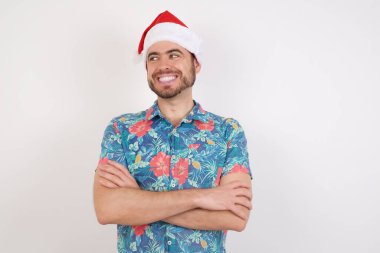 Noel Baba şapkalı genç adam kollarını kavuşturuyor, iyi görünüyor. 