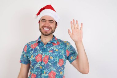 Noel Baba şapkalı genç adam el sallıyor. Mutlu ve gülümsüyor. Hoş geldin jesti..