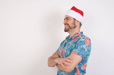 Noel Baba şapkalı genç adam kollarını kavuşturup yana bakıyor.  