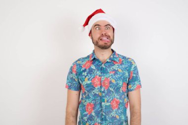 Noel Baba şapkalı genç adam suratını ekşitmiş, şaşı bakıyor ve dil gösteriyor. Komik ve çılgın olmak
