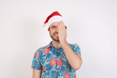 Noel Baba şapkalı genç adam bir gözünü eliyle kapatıyor, yüzünde kendine güvenen bir gülümseme ve şaşırtıcı bir duygu var..