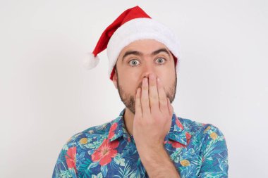 Noel Baba şapkalı genç adam şaşkınlıktan nefesi kesiliyor, ağzını avuç içi ile kapatıyor, kameraya şok olmuş gibi bakıyor. Tepki konsepti.