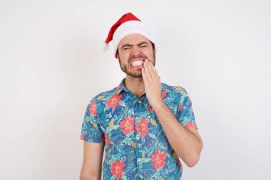 Noel Baba şapkalı genç adam diş ağrısı ya da diş hastalığından dolayı acı dolu bir ifadeyle ağzına dokunuyor..