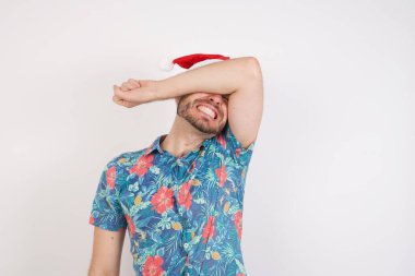 Noel Baba şapkalı genç adam kollarıyla gözlerini kapatıyor neşeli ve komik gülümsüyor. Kör kavram.