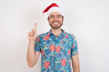 Noel Baba şapkalı genç adam bir numarayı gösterip işaret ederken kendinden emin ve mutlu bir şekilde gülümsüyor..