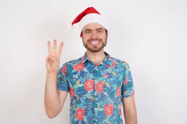 Noel Baba şapkalı genç adam üç numarayı gösterip işaret ederken kendinden emin ve mutlu gülümsüyor..