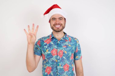 Noel Baba şapkalı genç adam kendini beğenmiş ve mutlu bir şekilde gülümserken dört numarayı gösteriyor ve işaret ediyor..
