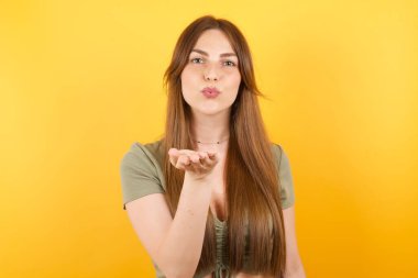 Güzel, genç bir kadın, kameraya bakıp havada bir öpücük savuruyor. Sevimli ve seksi. Aşk ifadesi.