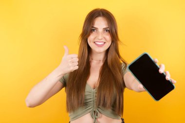 Sarı stüdyo arka planında poz veren güzel genç bir kadın.