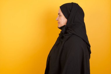 Sarı stüdyo arkasında poz veren tesettür takan güzel olgun bir kadın.