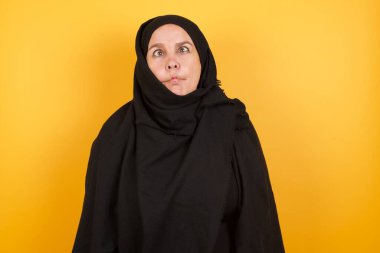 Sarı stüdyo arkasında poz veren tesettür takan güzel olgun bir kadın.