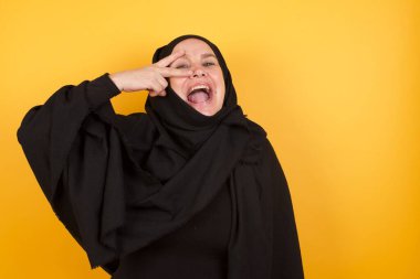 Başörtüsü takan olgun bir kadın barış sembolü yapıyor. Yüzünde parmaklar, gülümseyerek zaferi gösteriyor.