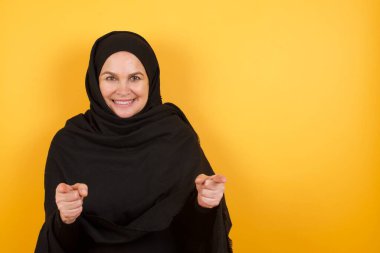 Olgun bir kadın tesettürlü, parmaklarıyla kamerayı işaret eden mutlu ve komik yüzlü. İyi enerji ve titreşimler. 