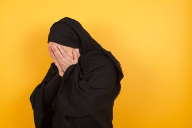 Stüdyoda ağlayan Müslüman kadın elleriyle yüzünü kapatıyor, siyah başörtüsü takıyor.