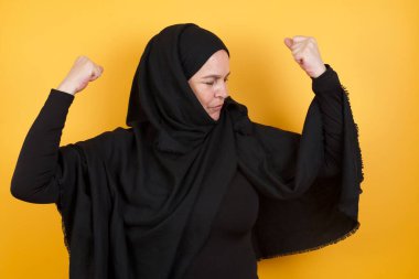 Sarı stüdyo arkasında poz veren tesettür takan güzel olgun bir kadın.