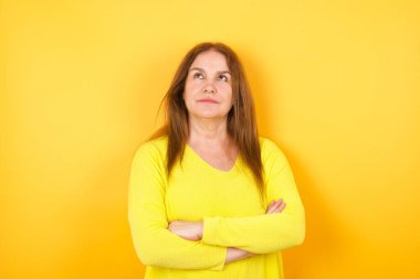 Neşeli, pozitif, hoş, hoş bir kadının fotoğrafı. Boş alana bakıyor. Sarı arka planda, düşünceli, izole edilmiş.