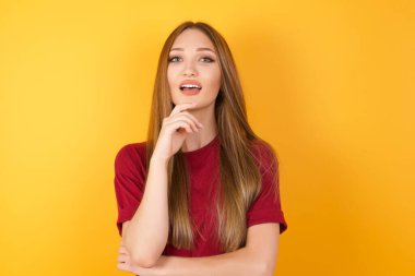 Güzel genç bir kadın ellerini kısmen çapraz yapar ve ellerini çenesinin altına sokar. Kameraya zevkle bakar. Mutlu duygu konsepti.