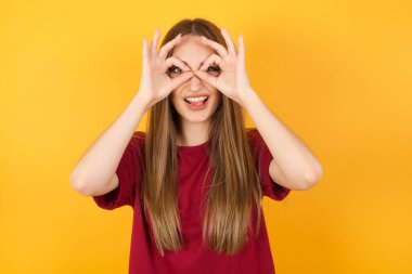 Güzel, genç bir kadın dürbün gibi jest yapıyor. Dilini dışarı çıkarıyor, gözleri parmaklarından bakıyor. Çılgın ifade.