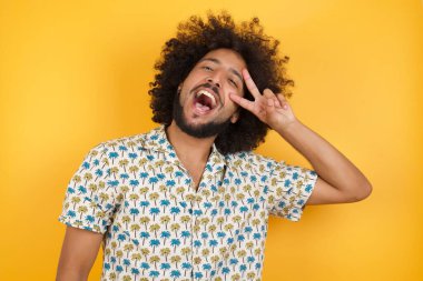 Yakışıklı genç adam barış sembolü yapıyor. Yüzünde parmaklar, gülümseyerek zaferi gösteriyor.