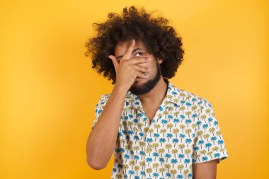 Yakışıklı genç adam şok içinde yüzünü ve gözlerini kapayarak utanmış bir ifadeyle parmaklarının arasından bakıyor..