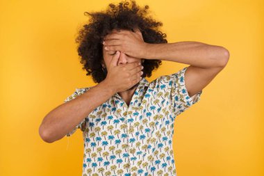 Yakışıklı genç adam elleriyle gözlerini ve ağzını kapatıyor, şaşırmış ve şok olmuş. Duyguları gizlemek.