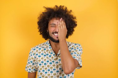 Yakışıklı genç bir adam bir gözünü eliyle kapatıyor, yüzünde kendine güvenen bir gülümseme ve şaşırtıcı bir duygu var..