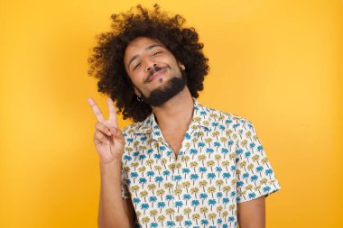 Yakışıklı, gülümseyen ve kameraya göz kırpan genç bir adam zafer işareti yapıyor. İki numara..