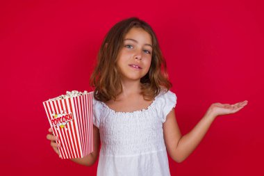 Kırmızı stüdyo arka planında patlamış mısırı olan tatlı küçük kız.