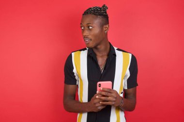 Kırmızı stüdyo arka planında akıllı telefon kullanan genç yakışıklı adam.