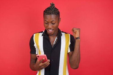 Kırmızı stüdyo arka planında akıllı telefon kullanan genç yakışıklı adam.