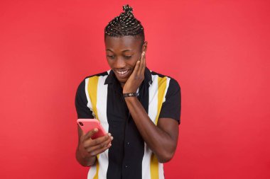 Kırmızı stüdyo arka planında akıllı telefon kullanan genç yakışıklı adam.