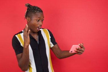 Kırmızı stüdyo arka planında akıllı telefon kullanan genç yakışıklı adam.