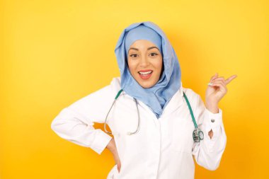 Sarı stüdyo arka planında steteskobu olan güzel bir kadın Arap doktor.