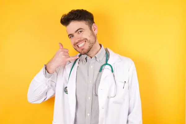 電話で話すような手や指で携帯電話のジェスチャーを行う笑顔医療制服を着て巻き毛の若いハンサムな医者の男 概念の伝達 — ストック写真