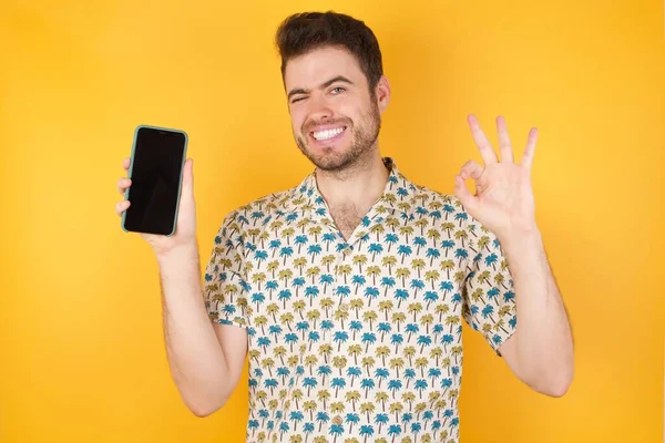 Homem Caucasiano Estúdio Segurando Telefone Celular Mostrando Sinal Com Dedos — Fotografia de Stock