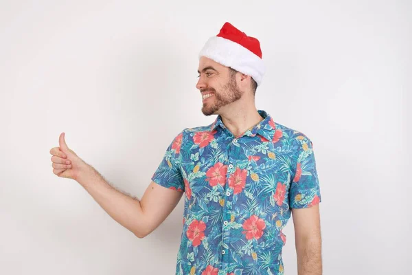 头戴圣诞礼帽的年轻人看起来很自豪 对着旁边做着竖起大拇指的手势 干得好 — 图库照片