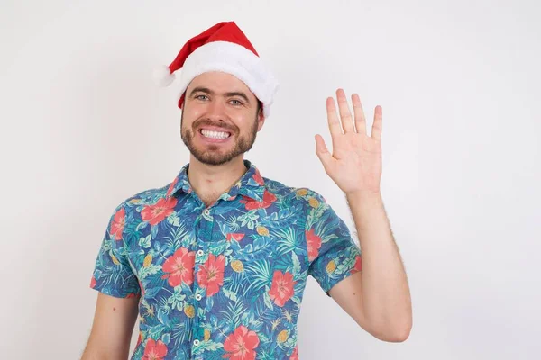 Noel Baba şapkalı genç adam el sallıyor. Mutlu ve gülümsüyor. Hoş geldin jesti..