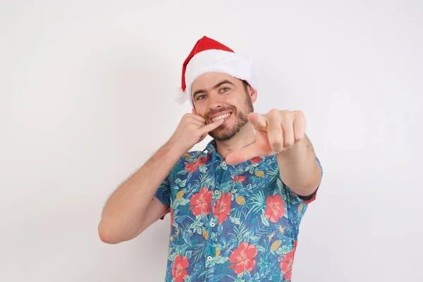 Noel Baba Şapkalı Genç Adam Neşeyle Gülümsüyor Kamerayı Işaret Ediyor — Stok fotoğraf