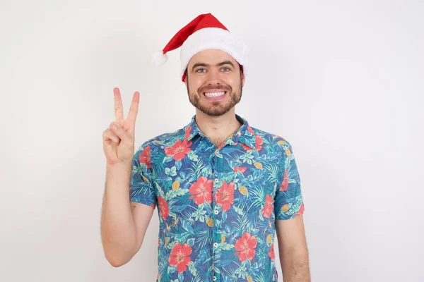Mladý Muž Klobouku Santa Ukazuje Ukazuje Prsty Číslo Dvě Usmívá — Stock fotografie