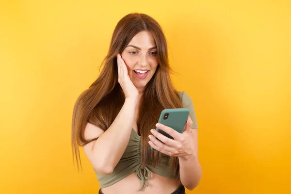 Krásná Mladá Žena Pózuje Moderním Smartphonem Žlutém Pozadí Studia — Stock fotografie