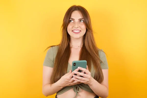 漂亮的年轻女子在黄色工作室背景下摆出一副现代智能手机的样子 — 图库照片