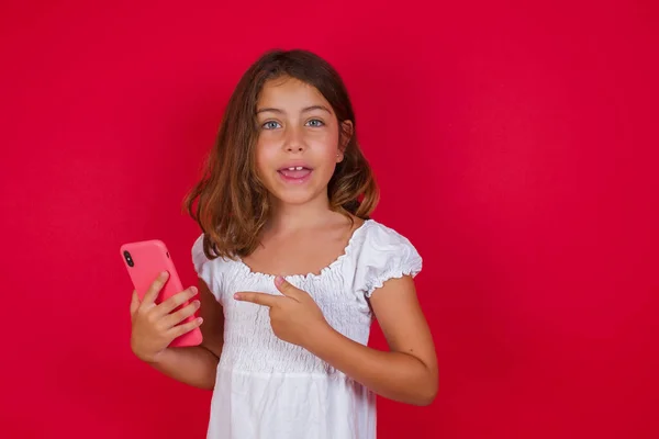 Schattig Klein Meisje Met Smartphone Poseren Rode Studio Achtergrond — Stockfoto