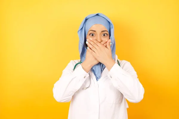 Νεαρή Γυναίκα Γιατρός Φορώντας Ιατρική Στολή Σοκαρισμένη Κάλυψη Στόμα Χέρια — Φωτογραφία Αρχείου