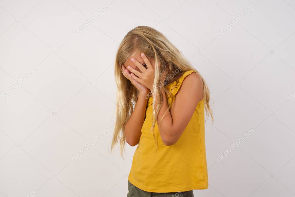 Sad cute little girl crying covering her face with her hands. 