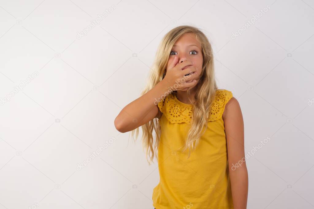 cute little girl  gasps from astonishment, covers opened mouth with palm, looks shocked at camera. Reaction concept.