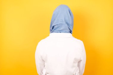 Tıbbi üniforma giyen genç bir doktorun sarı duvarın önünde duruşu. Stüdyo Çekimi.