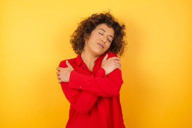 Güzel genç bir kadın mutlu ve olumlu bir şekilde kendine sarılıyor, kendinden emin gülümsüyor. Sevgi ve özgüven.