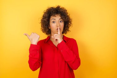 Güzel genç bir kadın sessiz olmak istiyor. Parmakları dudaklarında, elleri yana doğru uzanıyor. Sessizlik ve gizli konsept.