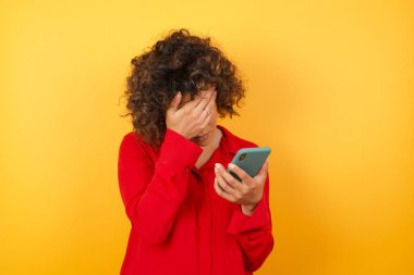 Stüdyoda elinde cep telefonu tutan üzgün bir kadın var. 